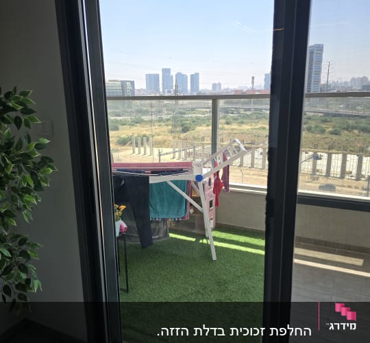 נוף עירוני מבעד לחלון זכוכית עם מרפסת ודשא סינתטי
